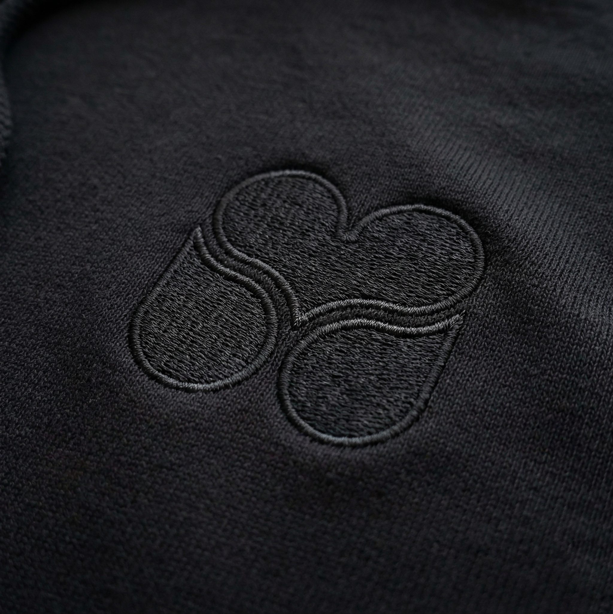 Close-up of Melriver embroidered icon on black hoodie chest